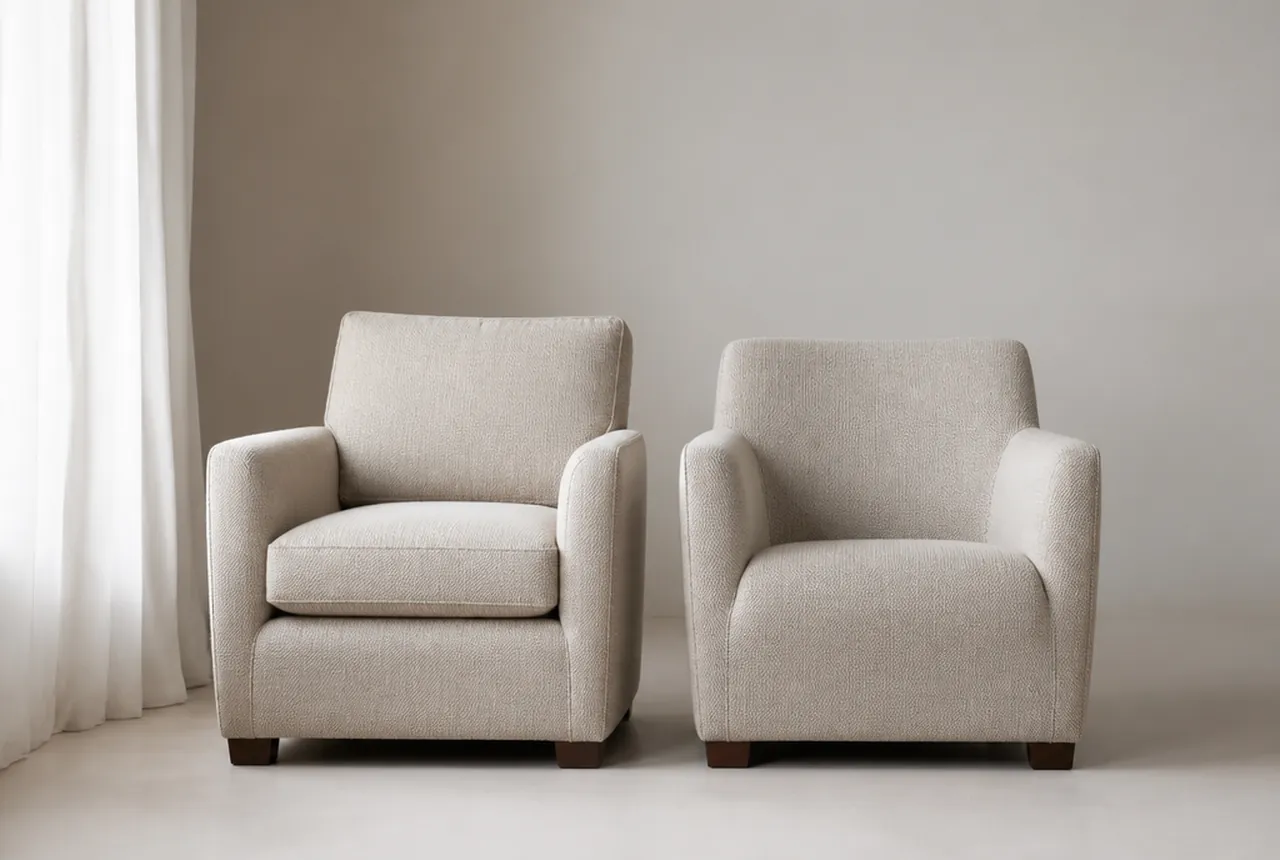 Two lounge chairs side by side on pale seamless, one with a removable seat cushion and one fully tight upholstered